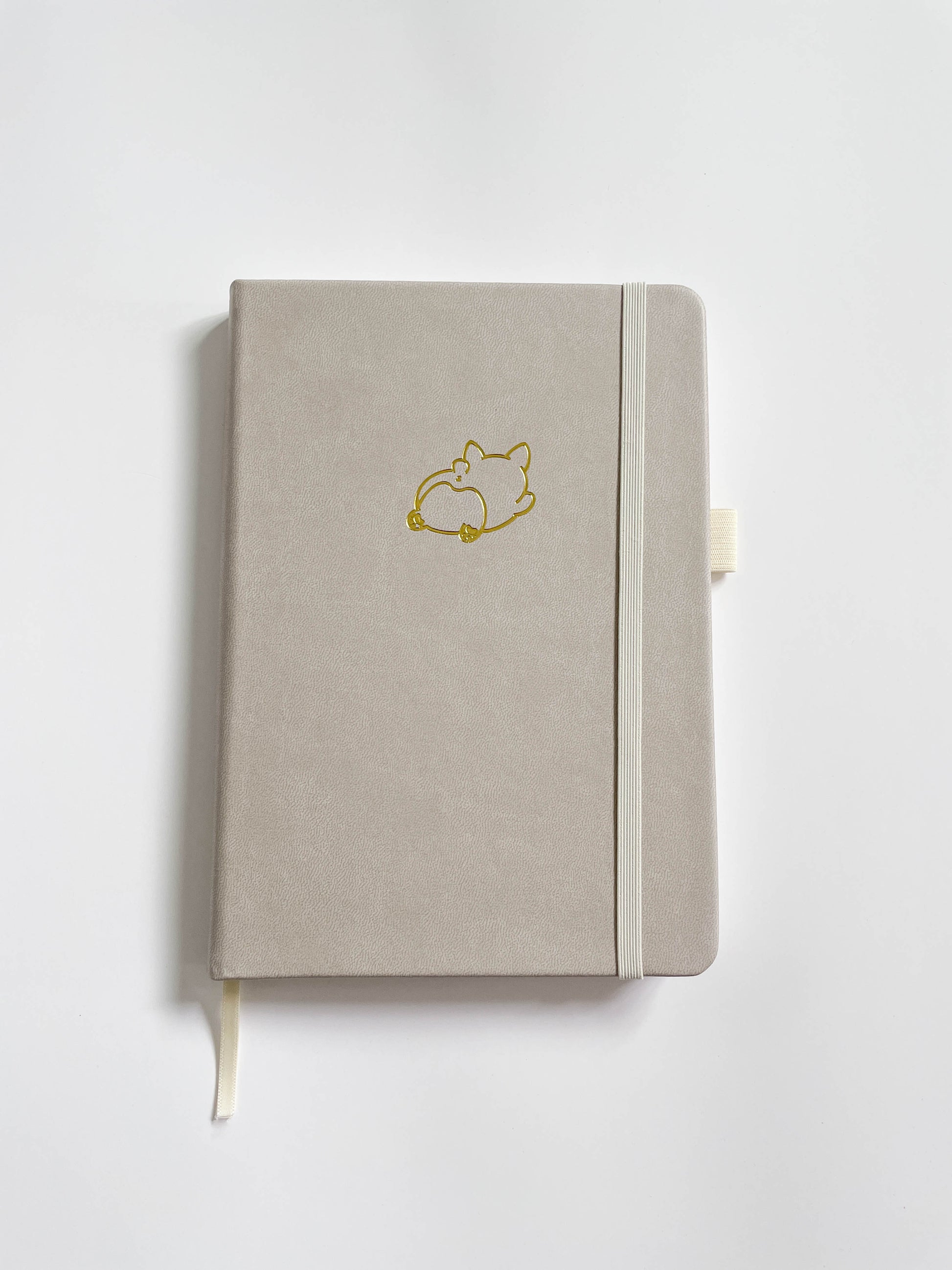 An ivory bullet journal with a gold foil embossed design of a chunky Corgi splooting.