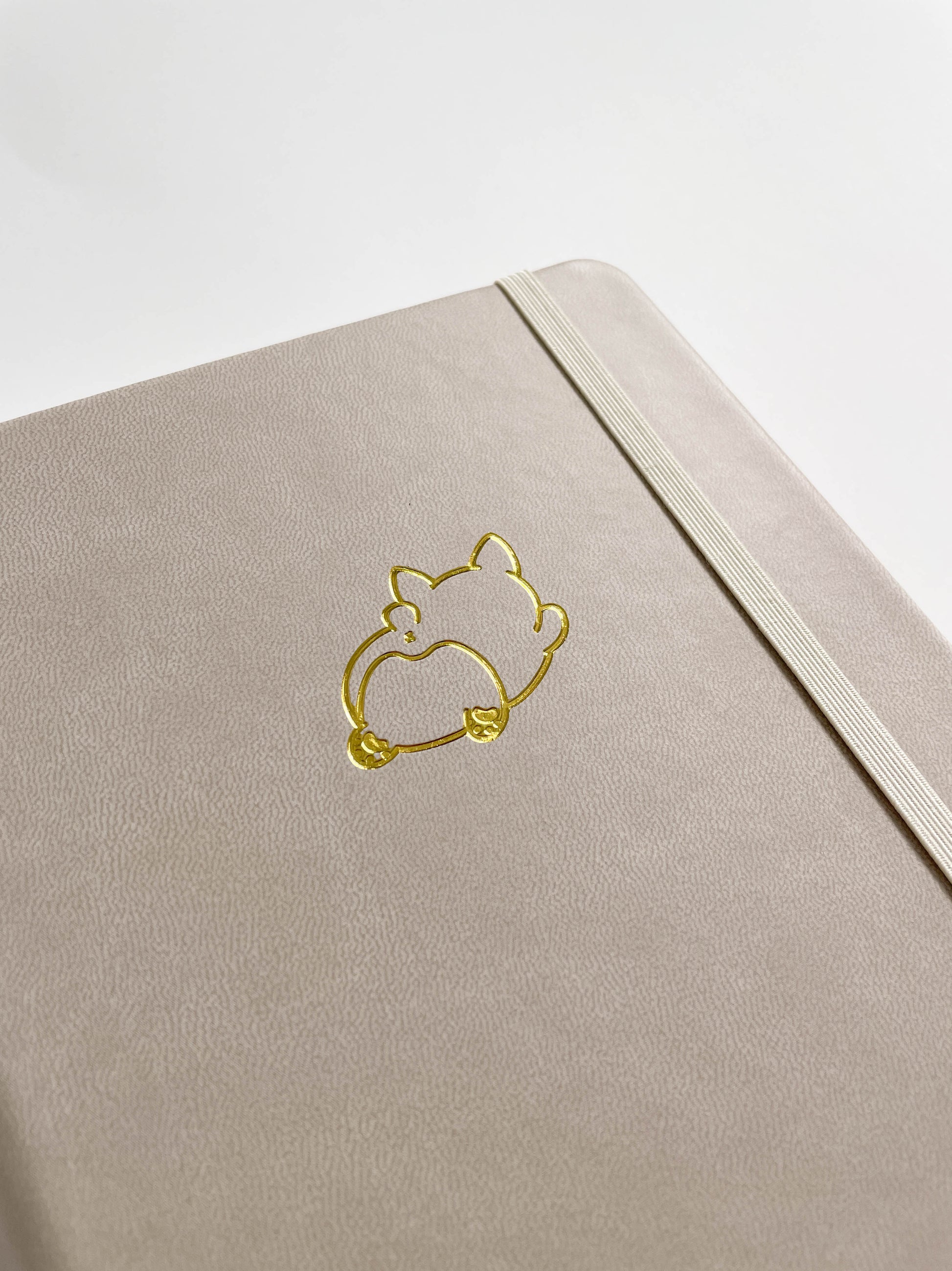 Close up view of the an ivory bullet journal with a gold foil embossed design of a chunky Corgi splooting.
