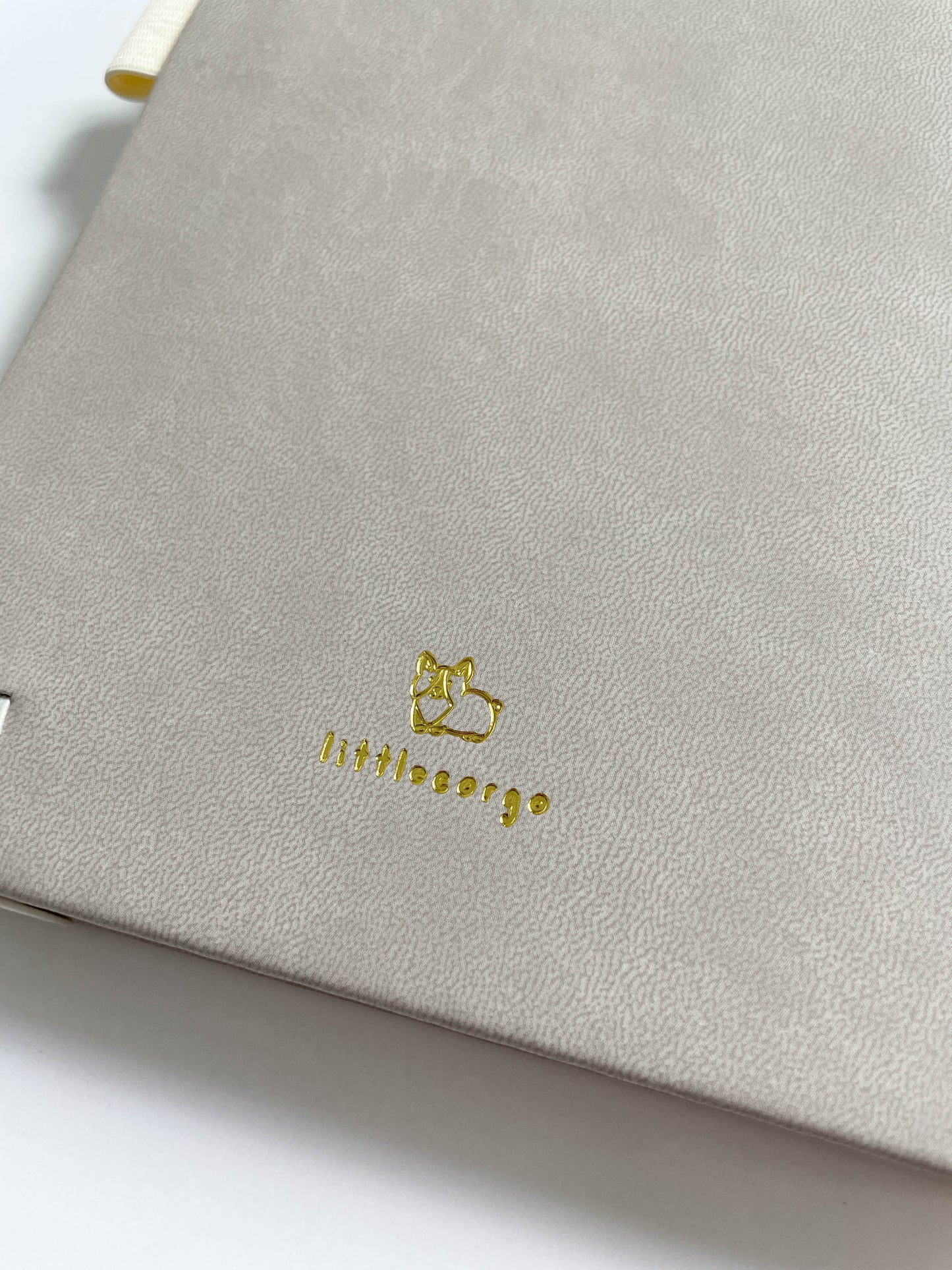 Close up view of the back of an ivory bullet journal's backside, specifically showing the gold foil embossed design of a Corgi and "littlecorgo" text.
